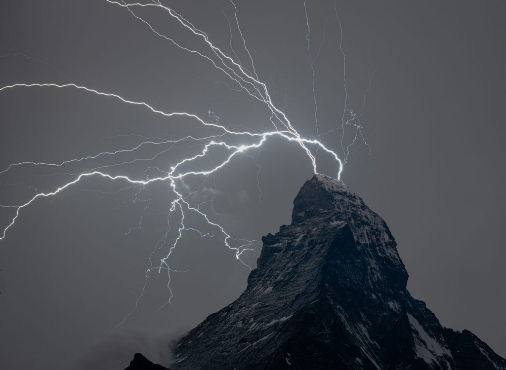 Numerous bolts of lightning appear immediately behind a massive, jagged mountain top